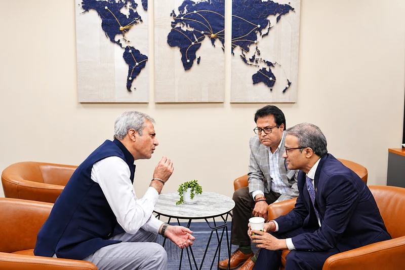 Three attendees converse around a table in the USICC Business Lounge beneath a world map.