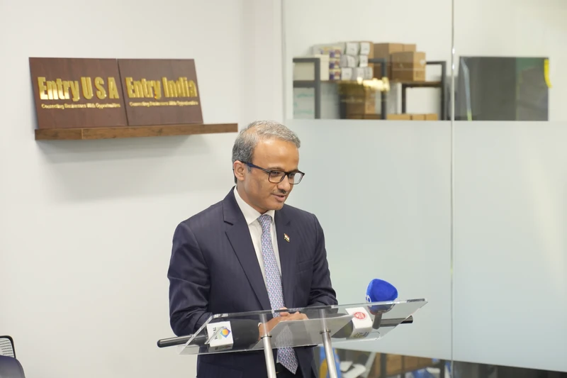 Ambassador Pradhan delivers his address at a clear lectern, with Entry USA and Entry India signs behind him.